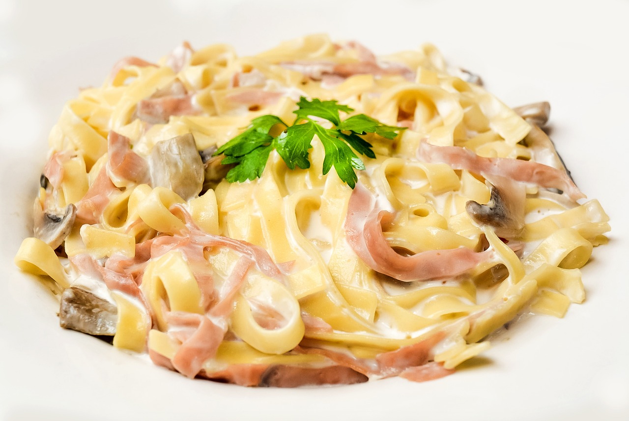 Pasta condita con panna e prosciutto, piatto appetitoso e colorato, servito in un piatto bianco.